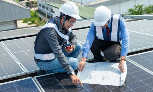 Engineers and solar panel technicians read installation location drawings and drill and install solar panels on the factory roof.